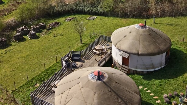 To yurts med træterrasser og siddeområder, omgivet af en indhegnet gård.