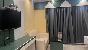 A modern hotel room with a flat-screen TV, a sofa, a small table with a coffee maker, and a curtain. - Royal Classic Hotel (Digha)