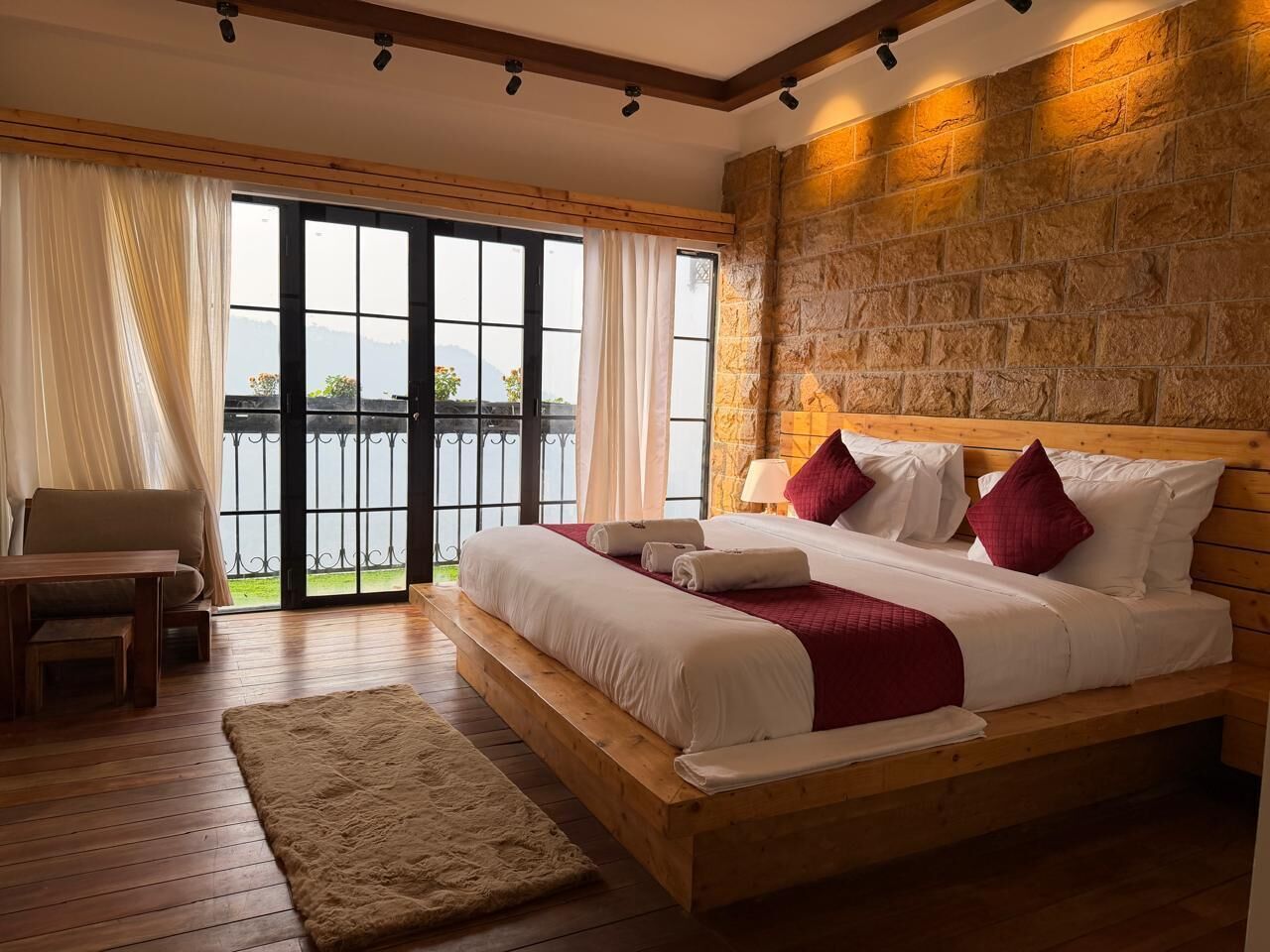 Een slaapkamer met een groot bed, een houten bankje, uitzicht door een glazen deur en een stenen muur.