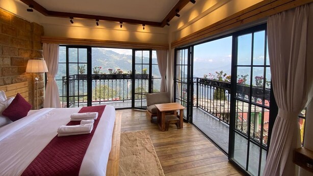 A hotel room with a large bed, a wooden floor, a balcony with a view, and a table with a chair. - Evri Hotels & Resorts (Kolakham)
