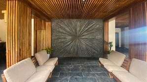 A reception area with a modern design, featuring a wooden slatted ceiling, a central stone wall with a radial pattern, and two beige sofas. - Evri Hotels & Resorts (Kolakham)