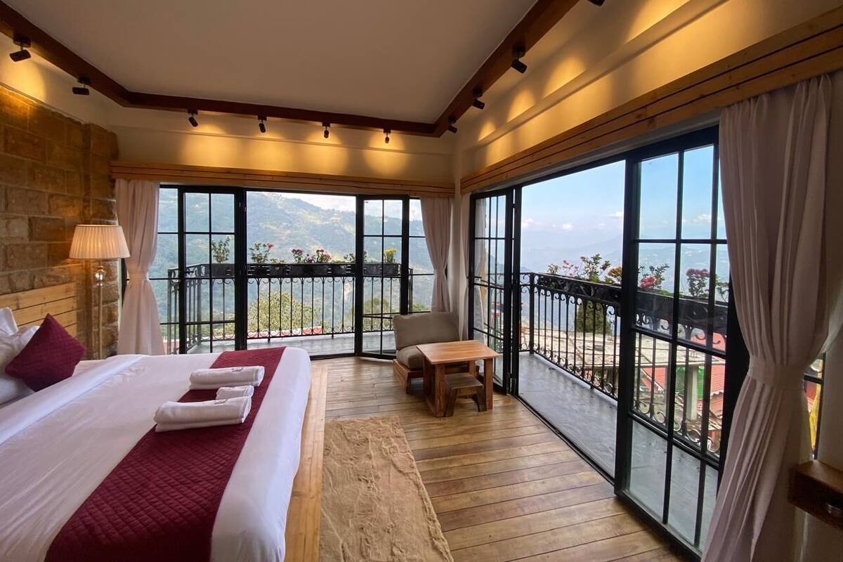 A hotel room with a large bed, a wooden floor, a balcony with a view, and a table with a chair.
