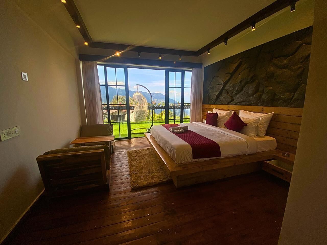 A bedroom with a large bed, wooden headboard, and a view of a green landscape through large windows.