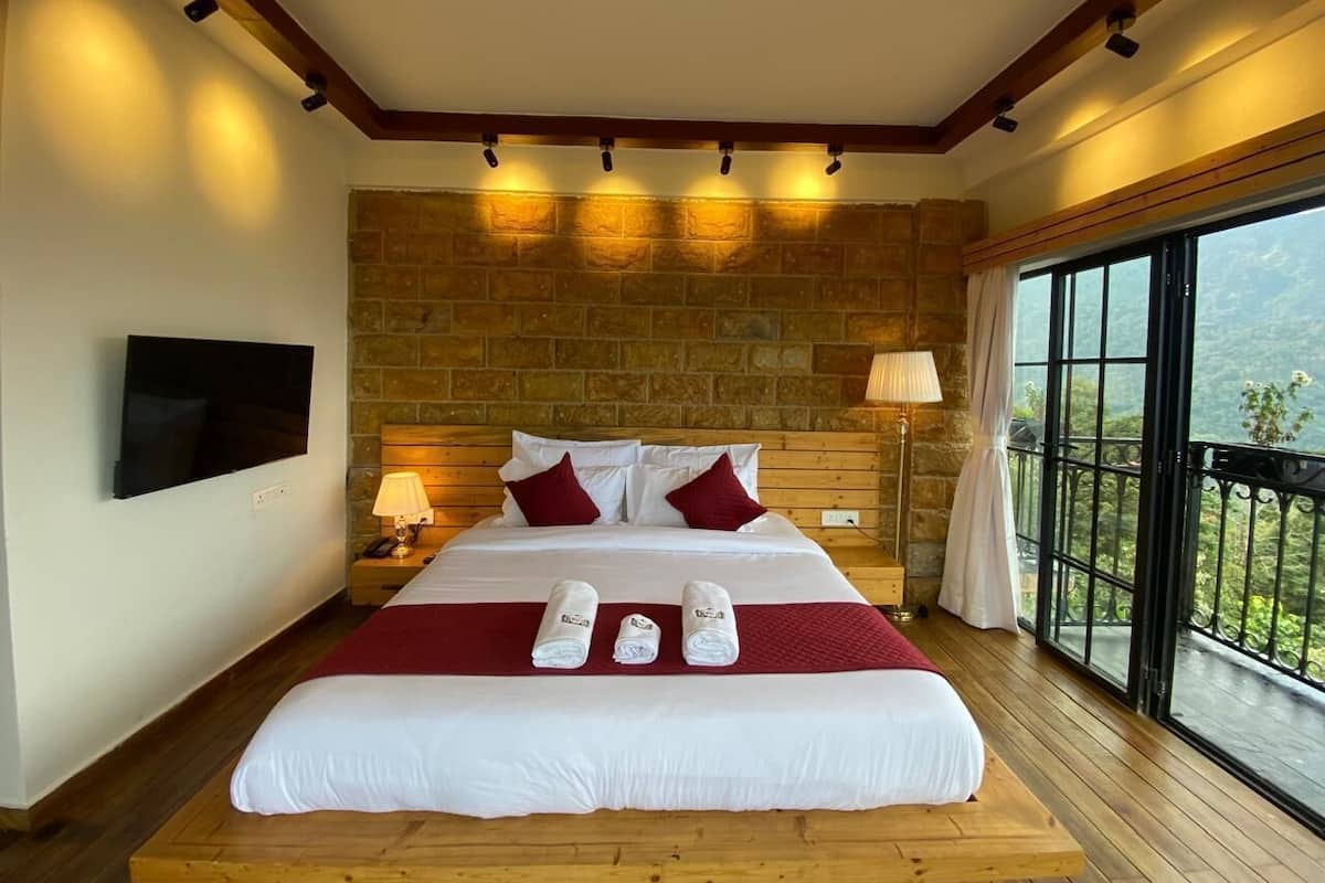 A hotel room with a large bed, a stone wall, a TV, a balcony with a view, and a wooden floor.