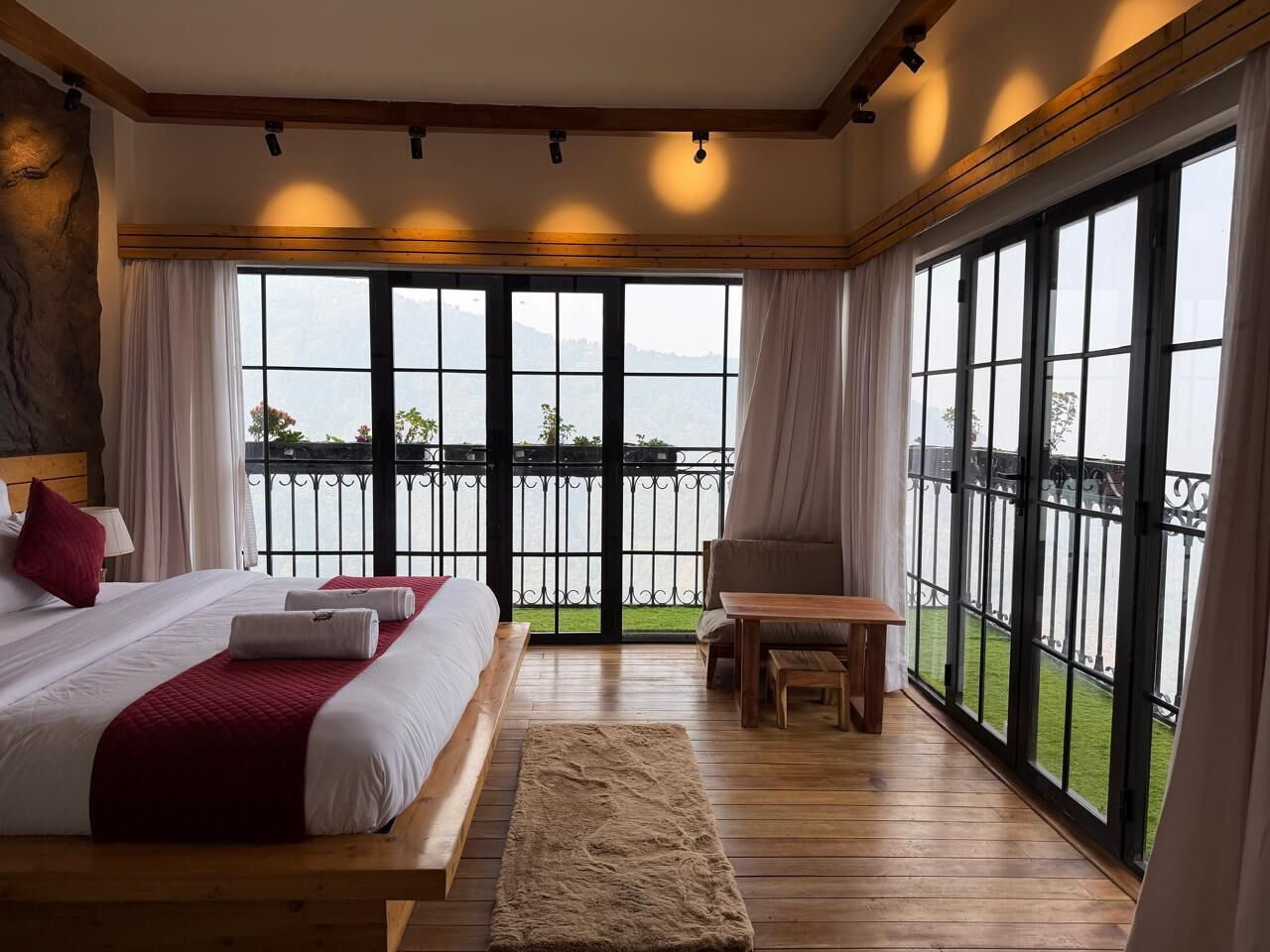 Une chambre à coucher avec un grand lit, un banc en bois et une vue sur une étendue d’eau, visible à travers de grandes fenêtres.