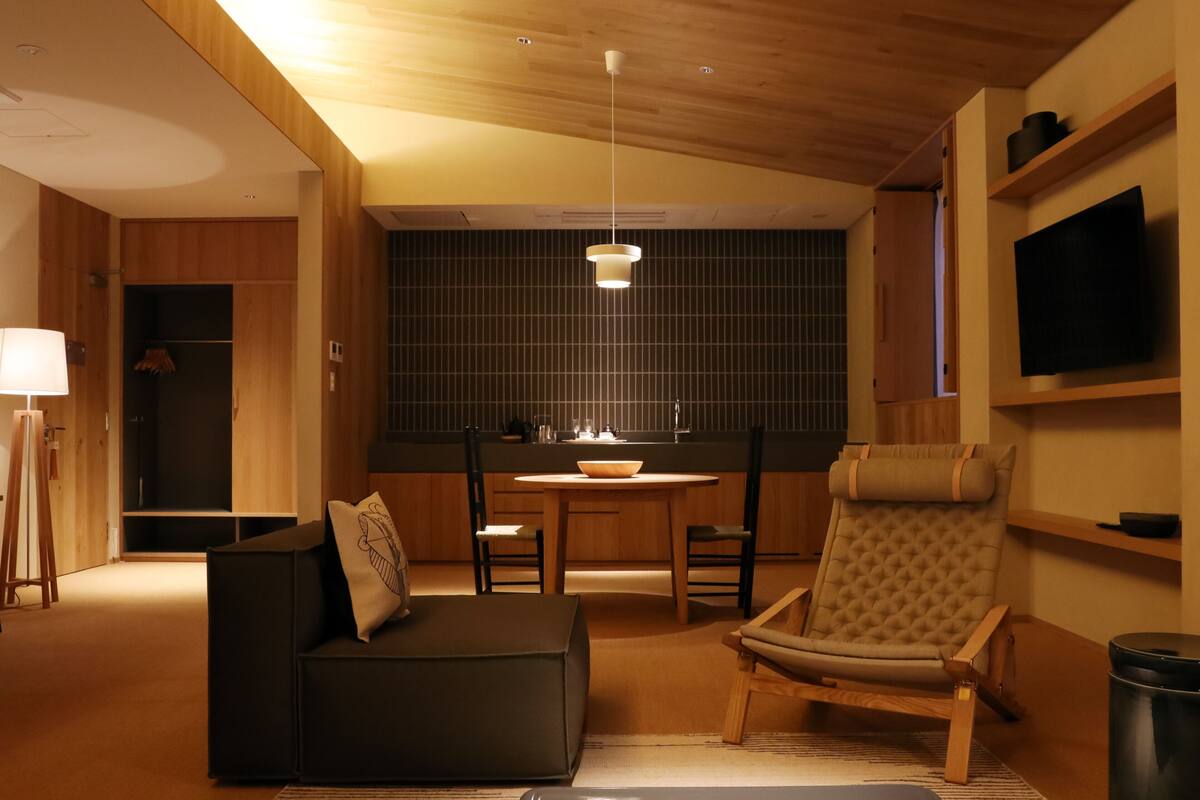 A modern living room with a sofa, armchair, dining table, and a TV mounted on the wall.