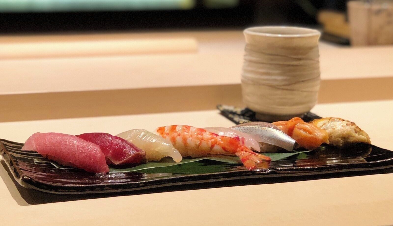 A black rectangular plate with various sushi pieces on a table.