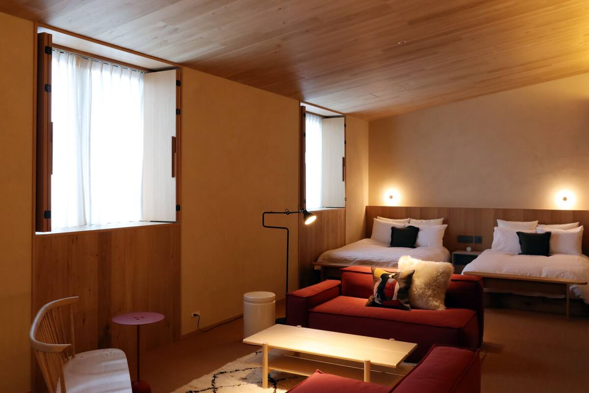 A room with a bed, a sofa, a small table, a chair, and a lamp.