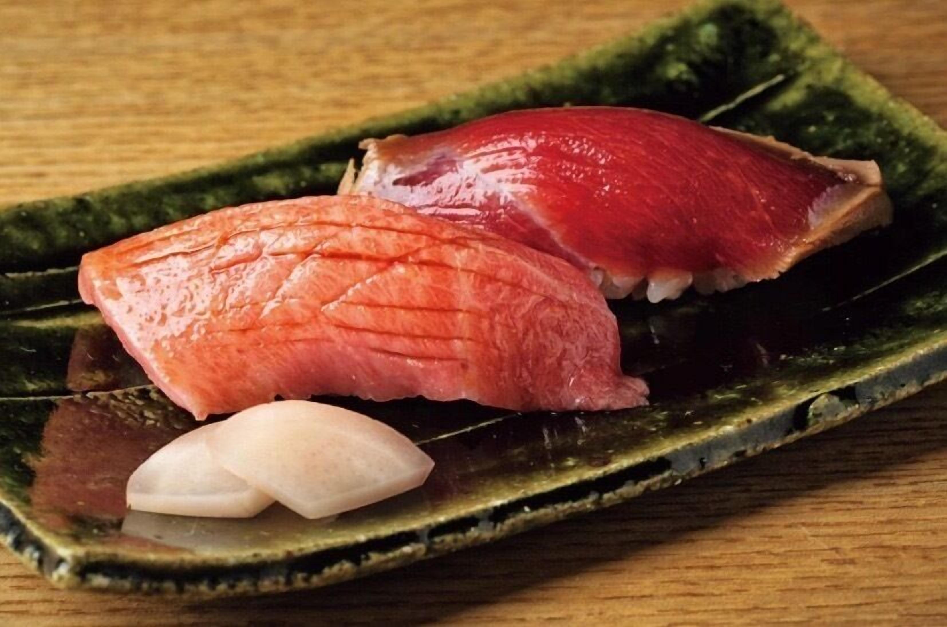 A plate with two pieces of sushi and two small white items on a green ceramic plate.
