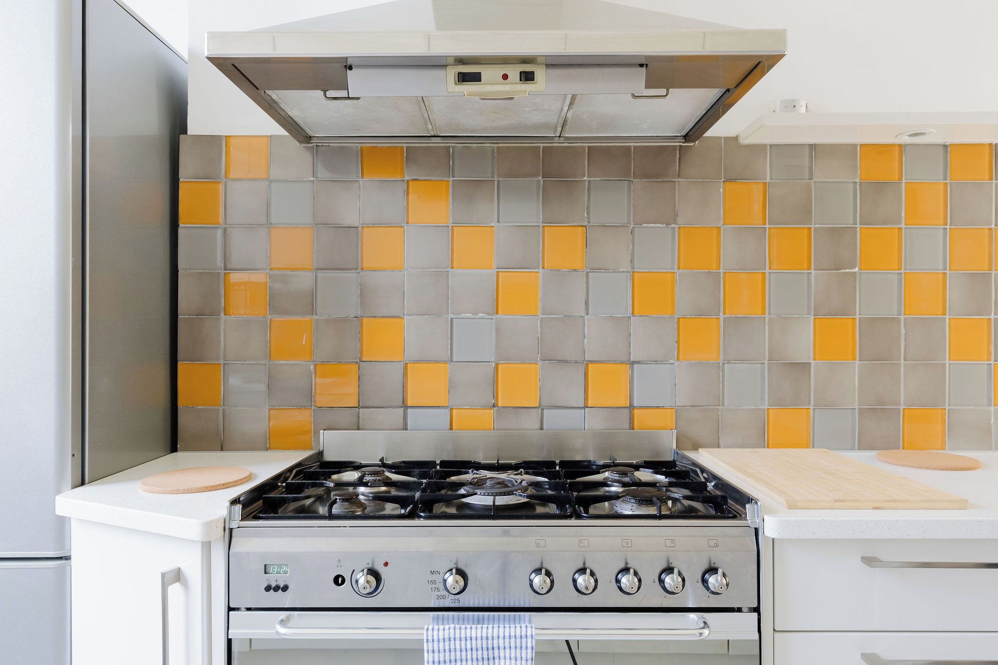 Een keuken met een gasfornuis, een afzuigkap en een betegelde spatwand.