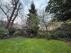 A grassy yard with a bench, trees, and a brick wall. - Spacious Sun Filled 1BDR Flat in Highbury (Greater London)