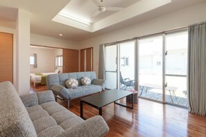 Ampla sala de estar com sofás, uma mesa de centro e uma porta de vidro deslizante que dá para um pátio externo.