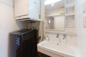 A bathroom with a black washing machine, a white sink, and a mirror above the sink. - ASHIBINA INN (Ishigaki)