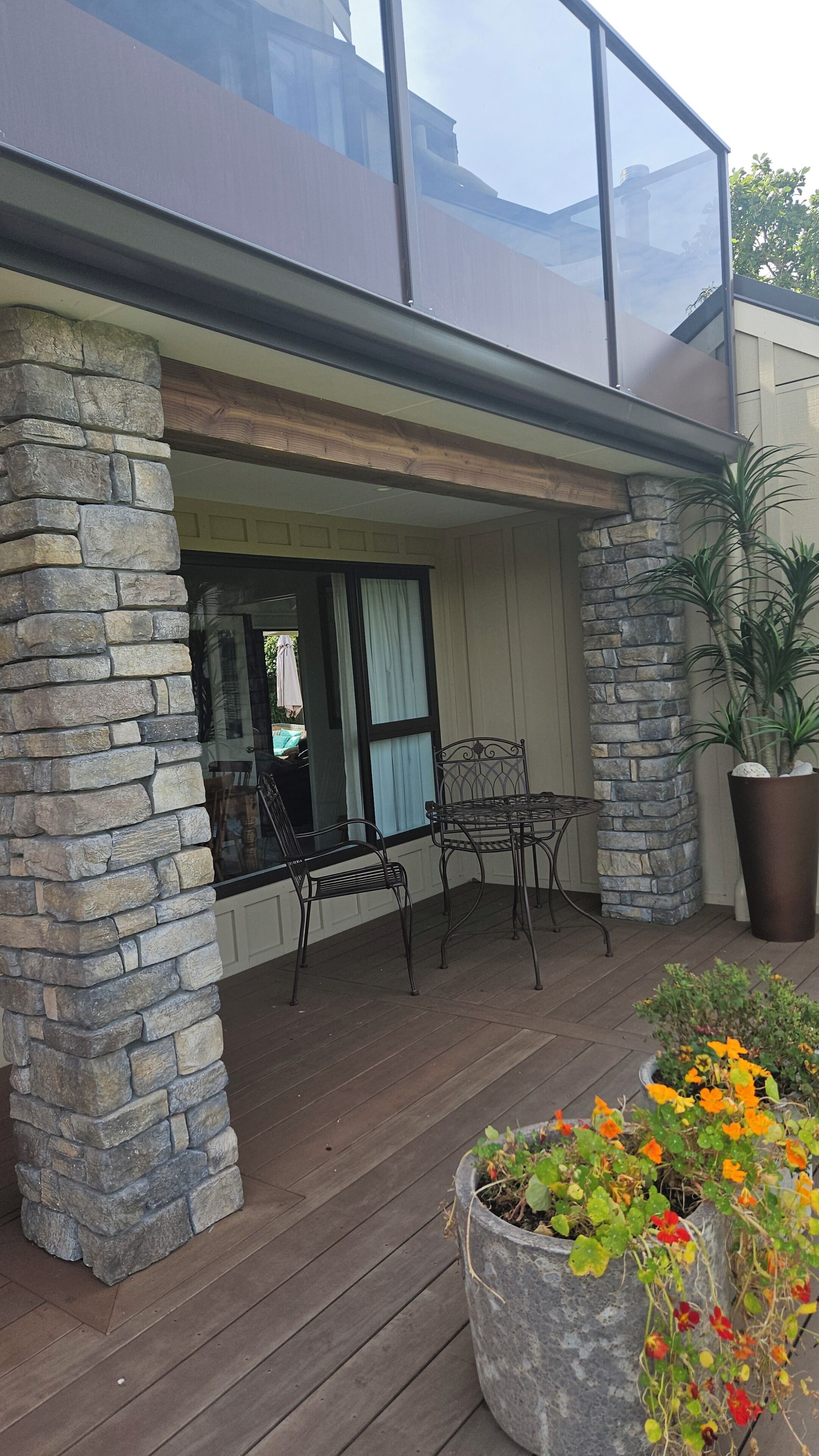 A modern house with a stone exterior, a covered patio with metal chairs, and a large potted plant.