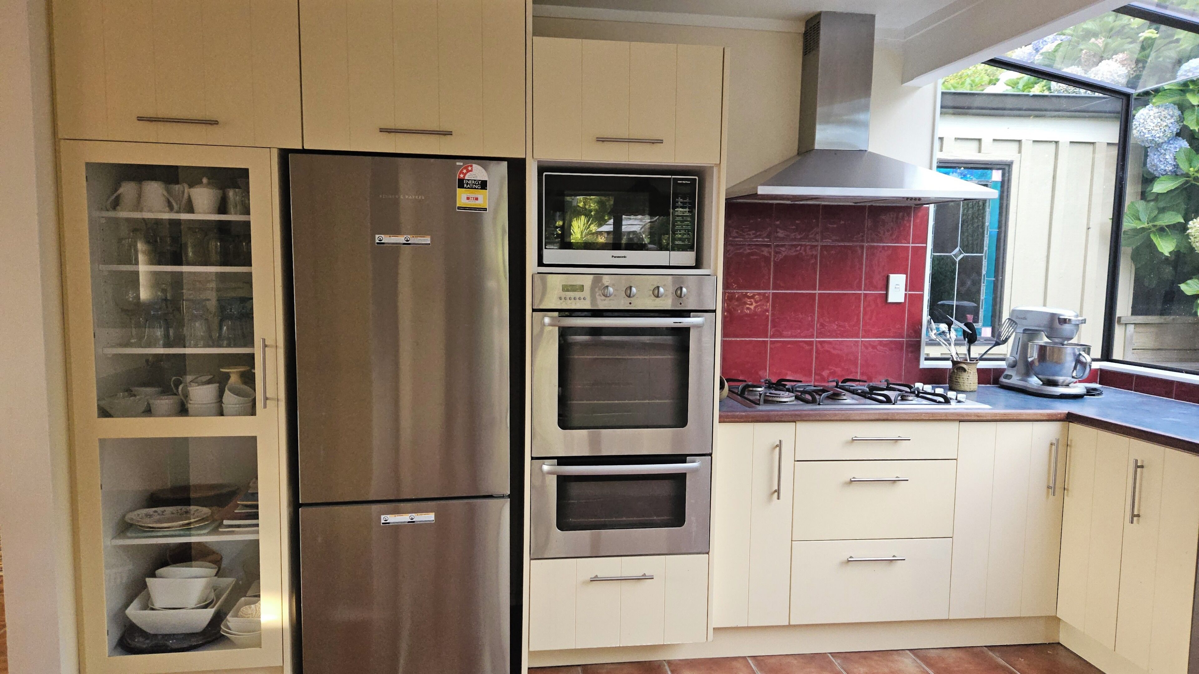 A kitchen with a stainless steel refrigerator, double oven, gas stove, and a red tiled backsplash.