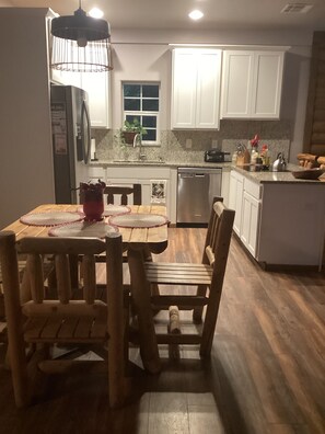 Une cuisine avec des chaises en bois, une table à manger, un réfrigérateur, un évier et des placards.