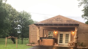 Una cabaña de madera con un jacuzzi, un porche y un cartel que dice 'BIENVENIDOS A CASA'.