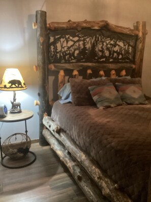 Un lit avec une tête de lit rustique, une lampe et une petite table sur laquelle est posé un objet décoratif.