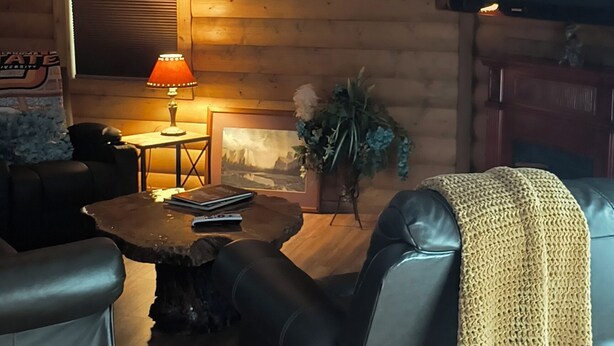 Una sala de estar acogedora con una pared de madera, un televisor de pantalla plana, un sofá de cuero, una mesa de centro y una lámpara.