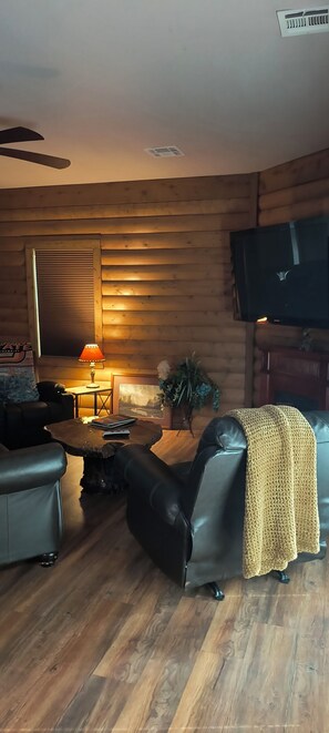 Ein gemütliches Wohnzimmer mit Holzwand, Flachbildfernseher, Ledersofa, Couchtisch und Lampe.