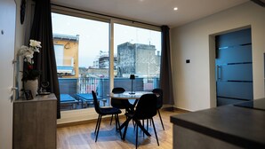 Ein moderner Essbereich mit einem runden Tisch, vier Stühlen, einer Zimmerpflanze und Blick auf die Stadt durch große Fenster.