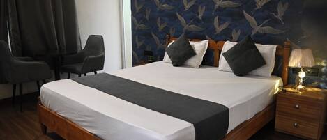 A hotel room with a large bed, a bedside table with a lamp, a chair, and a wall with a bird pattern.