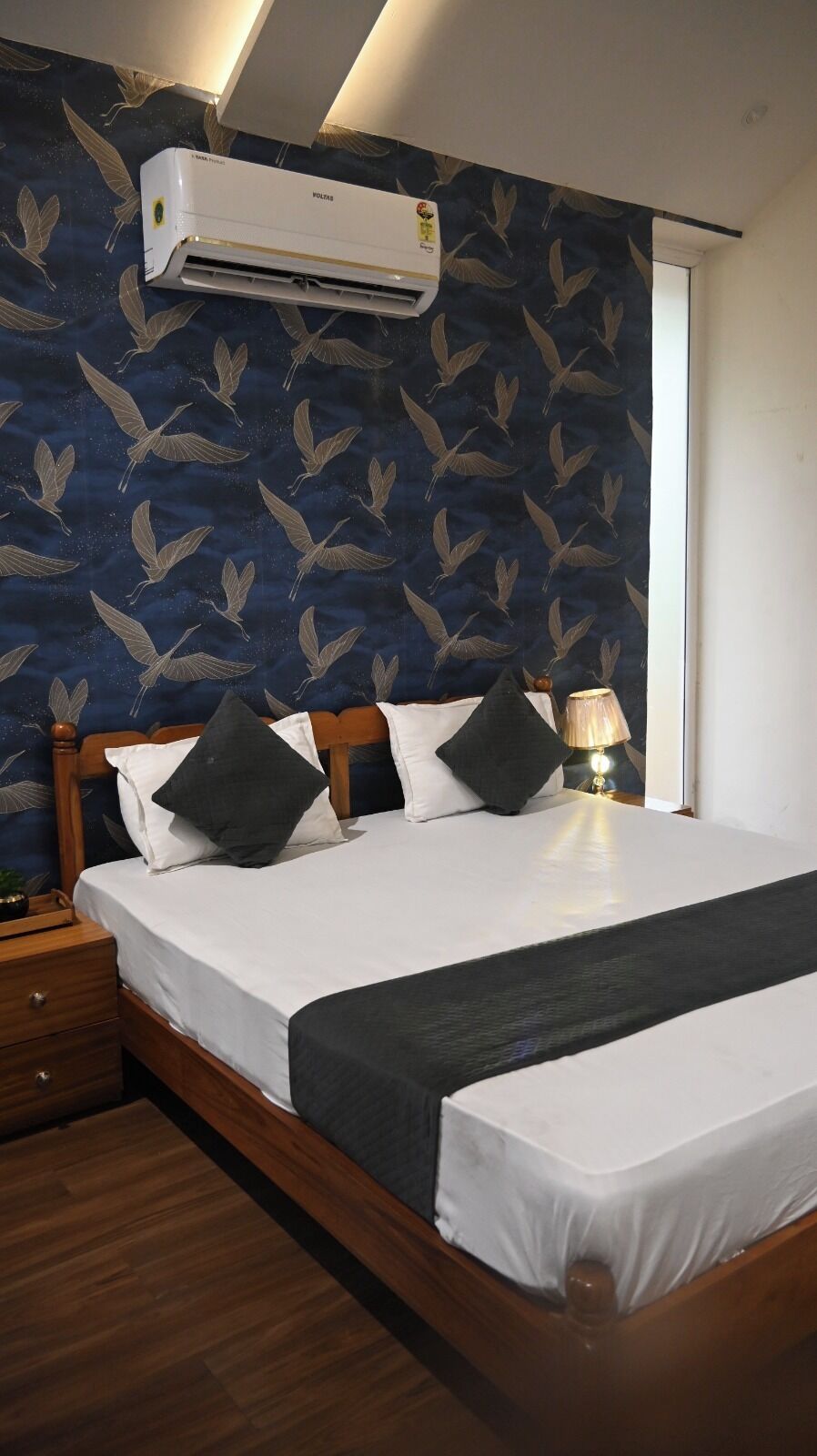 A hotel room with a bed, a nightstand, a lamp, and an air conditioner on the wall.