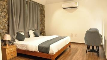 A bedroom with a bed, a desk, a chair, a lamp, and an air conditioner.