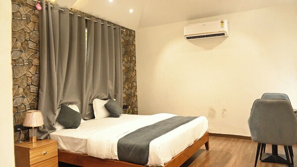 A bedroom with a bed, a chair, a nightstand, a lamp, and an air conditioning unit. - Butterfly Bliss Resort (Raigarh)