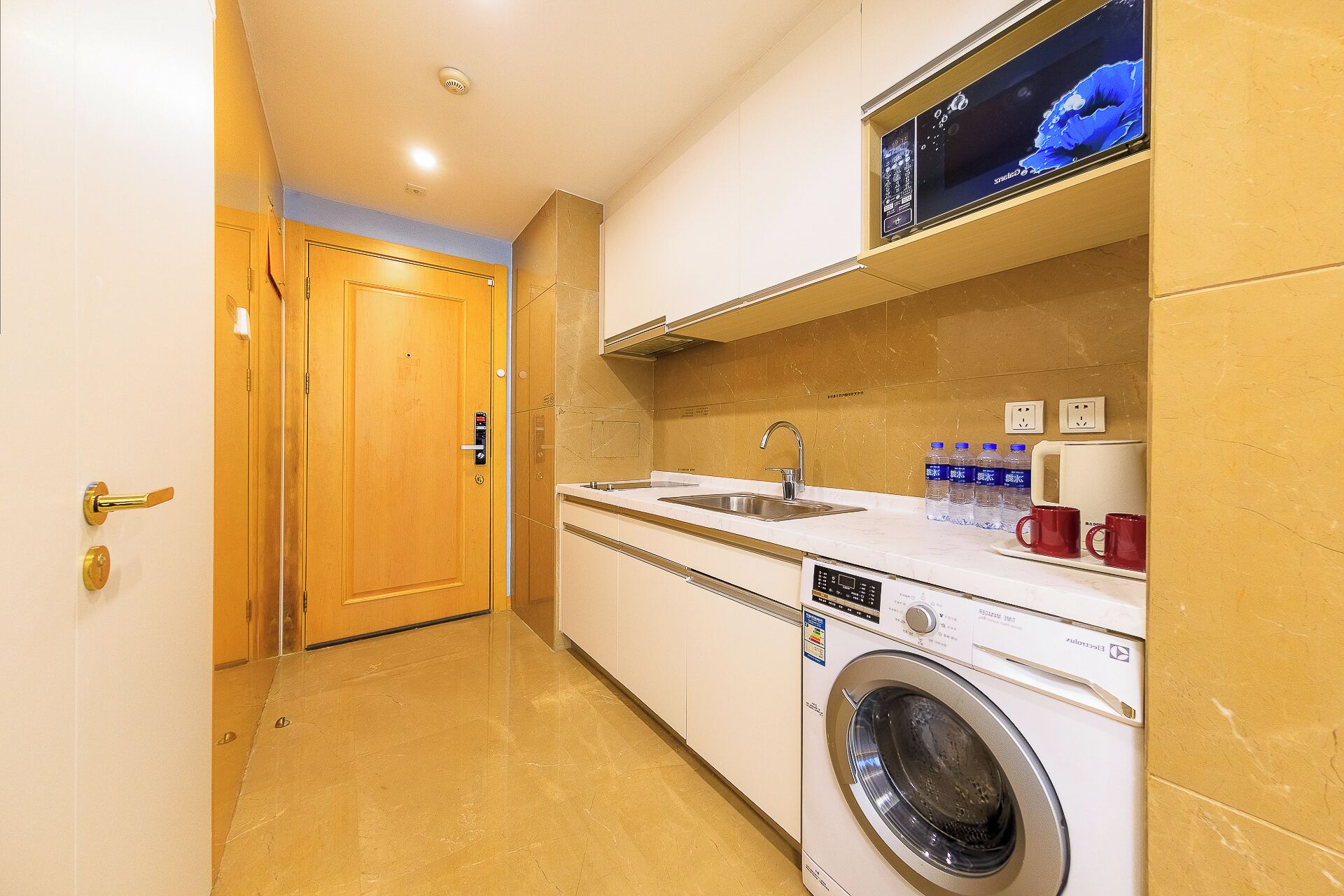 A compact kitchen with a washing machine, a sink, and a television mounted above the counter.