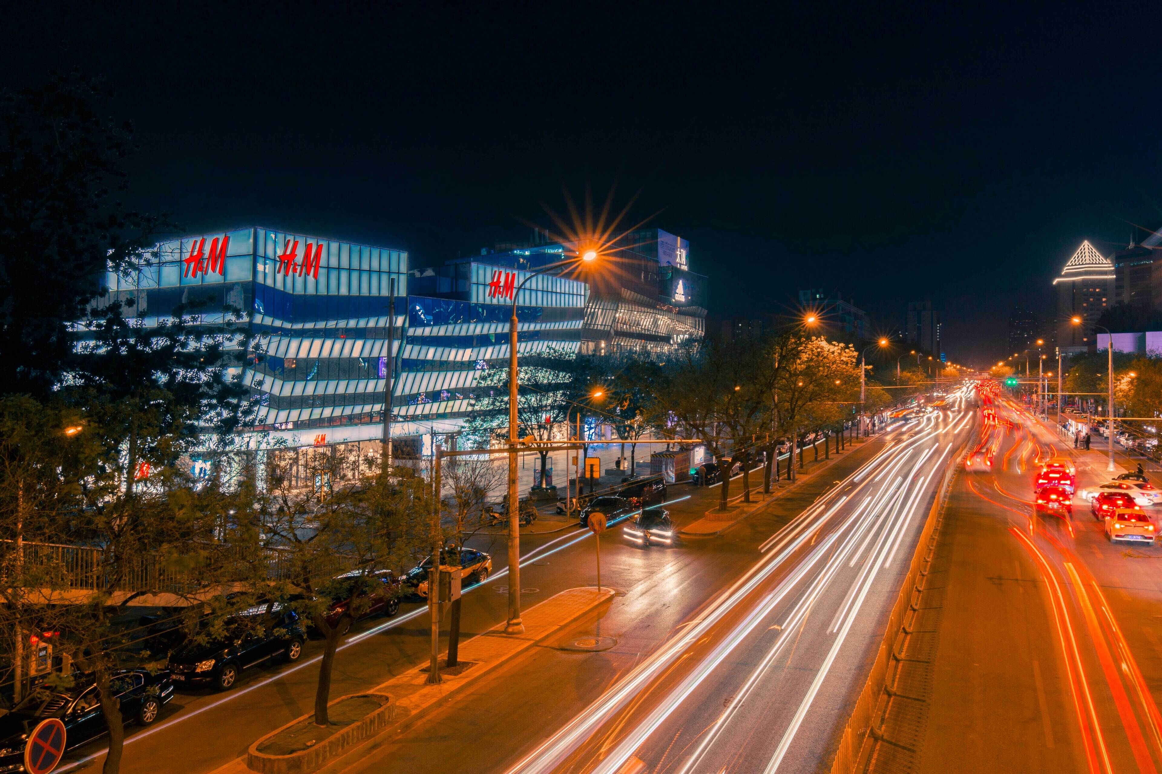 A multi-story building with illuminated signage, a wide road with light trails from vehicles, and a clear night sky.