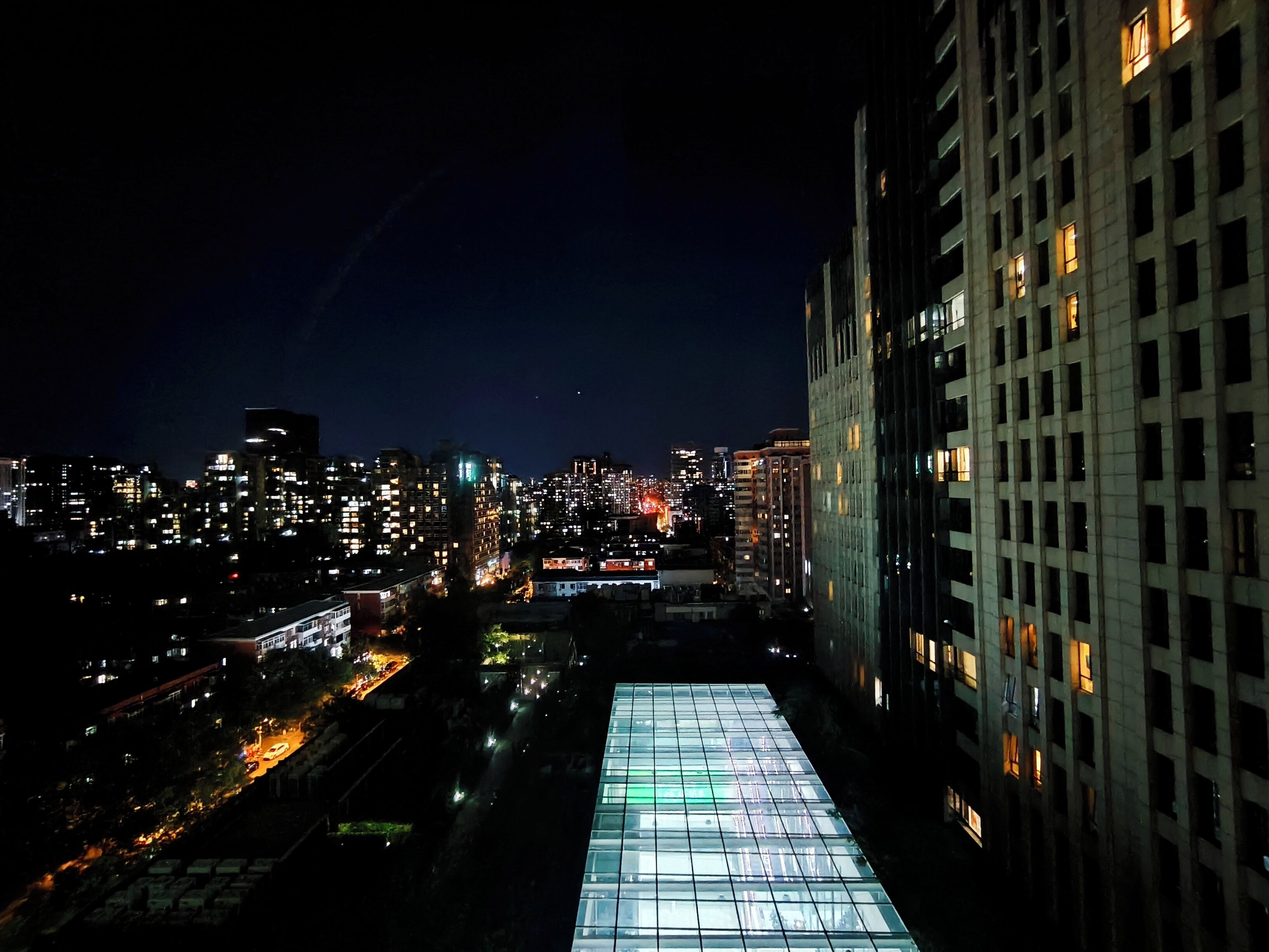 A nighttime cityscape with illuminated buildings and a prominent glass structure.