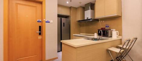 A compact kitchen with a wooden door, a built-in stove, a microwave, and a coffee maker.