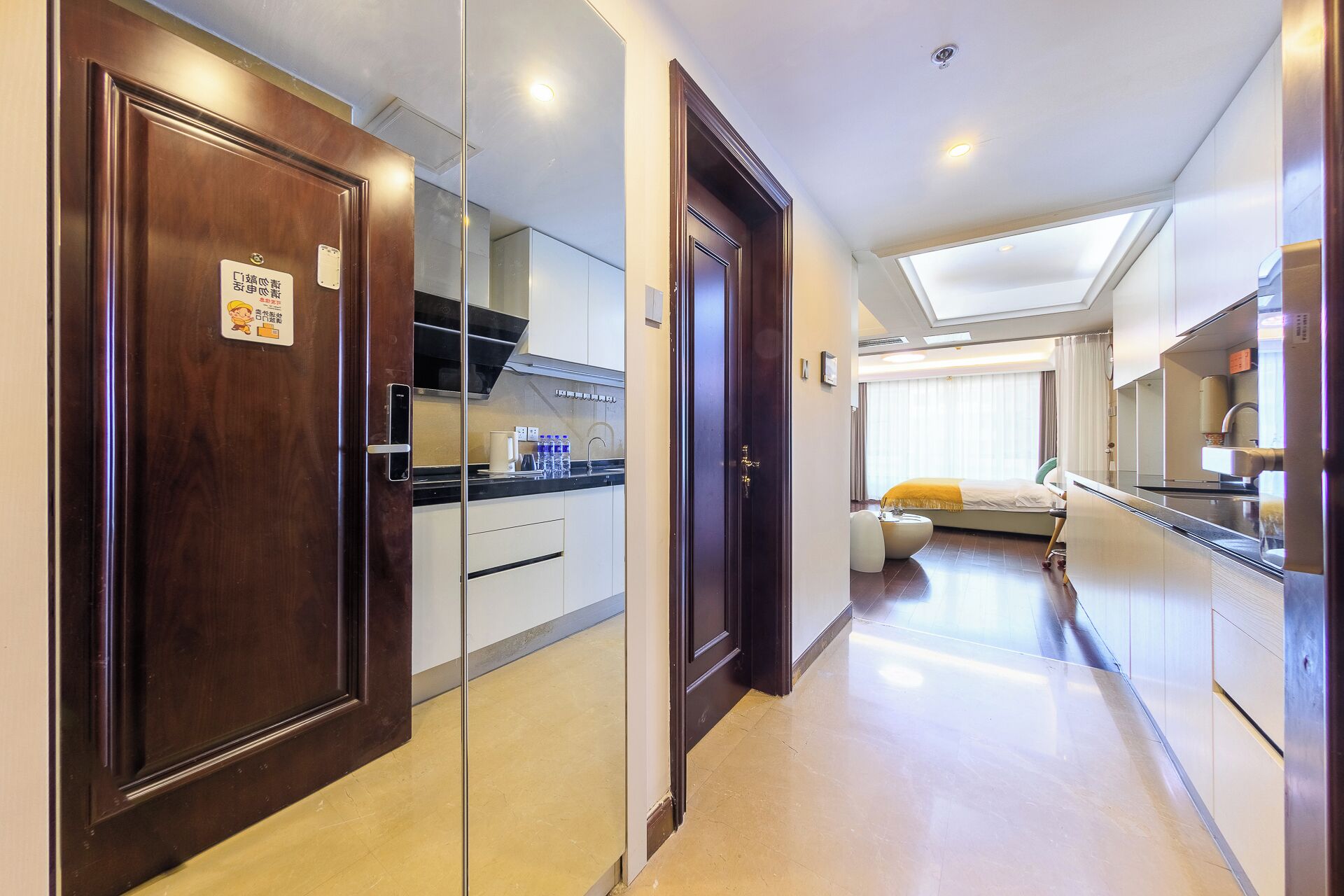 A hotel corridor with a kitchen area, a dining area, and a bedroom.