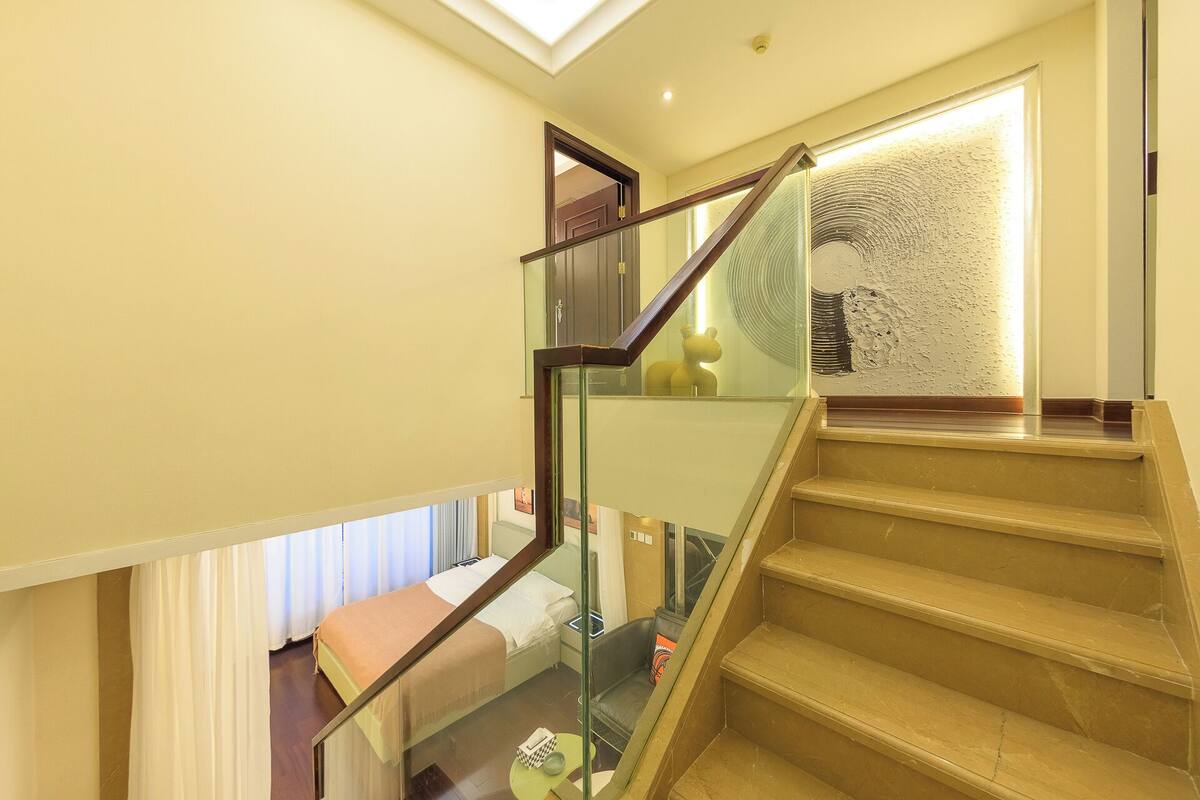 Un escalier avec des rampes en verre menant à une chambre à coucher équipée d’un lit et d’une table de chevet.