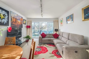 A living room with a sofa, a dining table with chairs, a TV, and artwork on the walls. - 2BDR Highgate Apt with Balcony and Free Parking (Greater London)