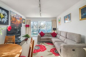 Ein Wohnzimmer mit einer Couch, einem Esstisch, Stühlen, einem Fernseher und Kunstwerken an den Wänden.