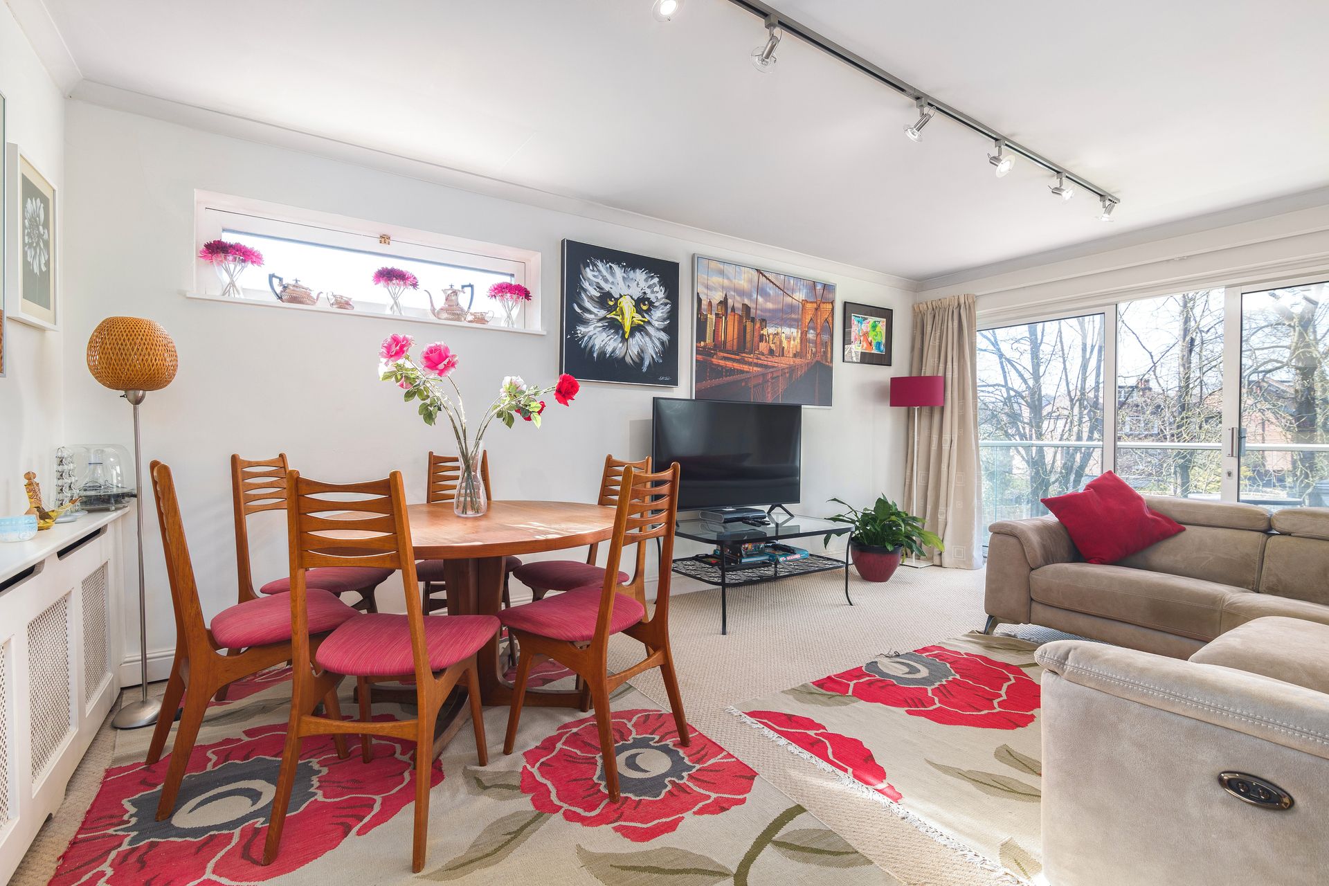 Un salon comprenant un téléviseur, un canapé, une table à manger avec des chaises et une grande fenêtre.