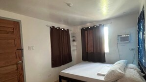 A bedroom with a bed, wooden floor, curtains, a ceiling fan, and an air conditioning unit.