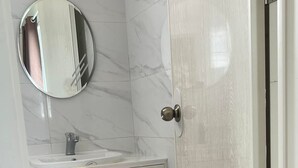 A bathroom with a marble sink, a mirror, a wooden door, and a small rug.
