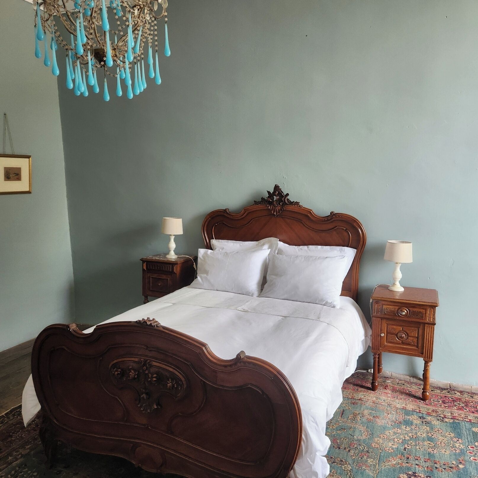 A bedroom with a wooden bed, two bedside tables, a chandelier, and a patterned rug.