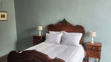 A bedroom with a wooden bed, two bedside tables, a chandelier, and a patterned rug.