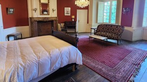 Une chambre à coucher avec un grand lit, une cheminée, un lustre et une fenêtre avec des volets.