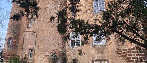 A historic stone castle with multiple windows, a central entrance, and surrounding greenery.