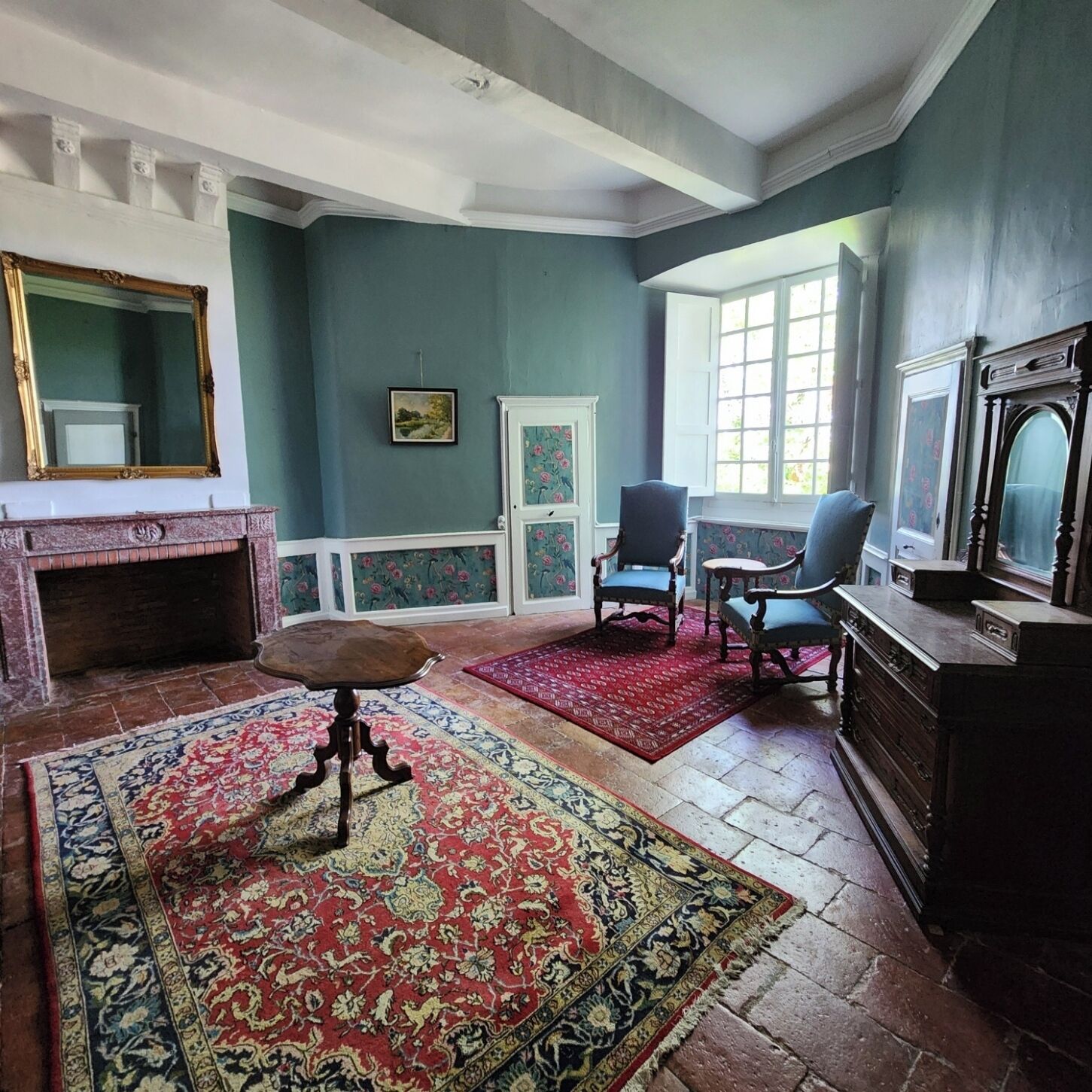 A room with a fireplace, a large rug, a chair, a television, and a window.