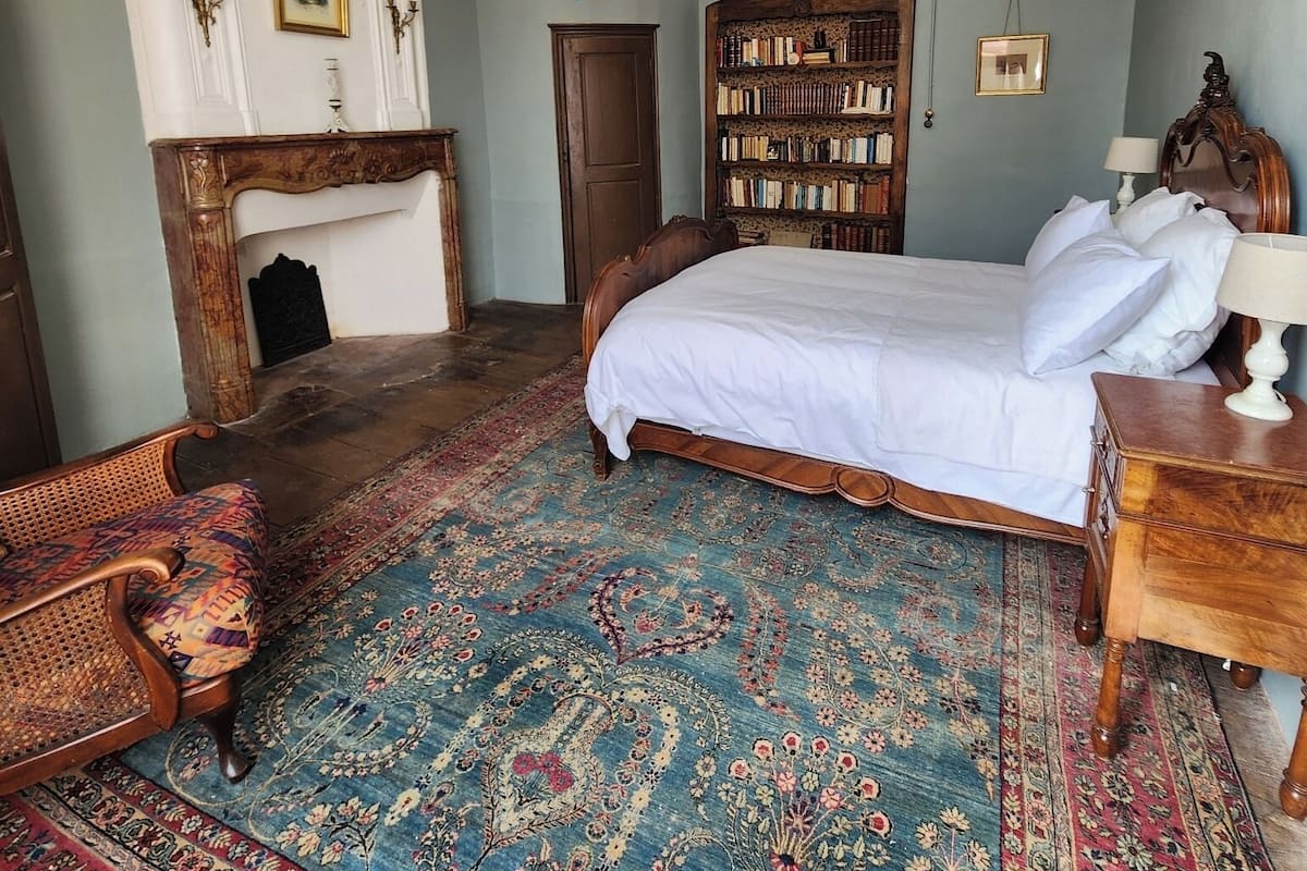 Une chambre avec un grand lit, une bibliothèque en bois, un lustre et un tapis à motifs.