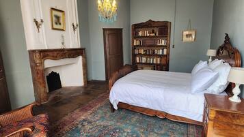 A bedroom with a large bed, a wooden bookcase, a chandelier, and a patterned rug.