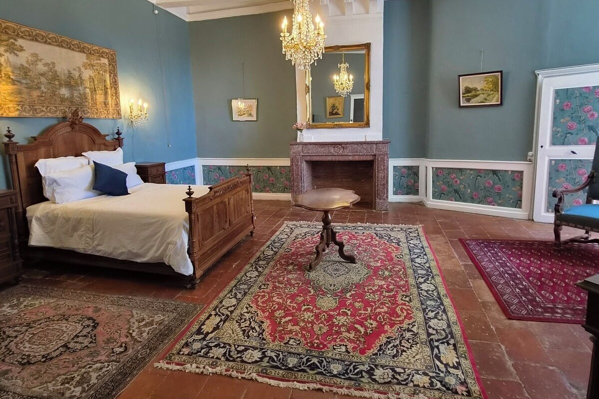 Ein Schlafzimmer mit einem Bett, einer Kandelaber, einem Kamin und einem großen Spiegel.