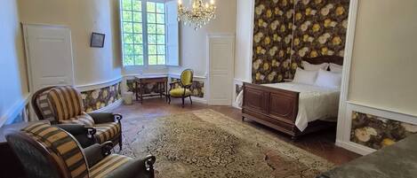 Ein Zimmer mit einem Bett, einem Sessel, einer Couch, einer Chandelier und einer Wand mit Muster.