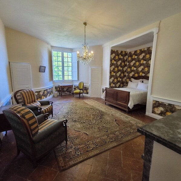 A room with a bed, a chair, a sofa, a chandelier, and a patterned wall. - Château de Trévien (Trévien)